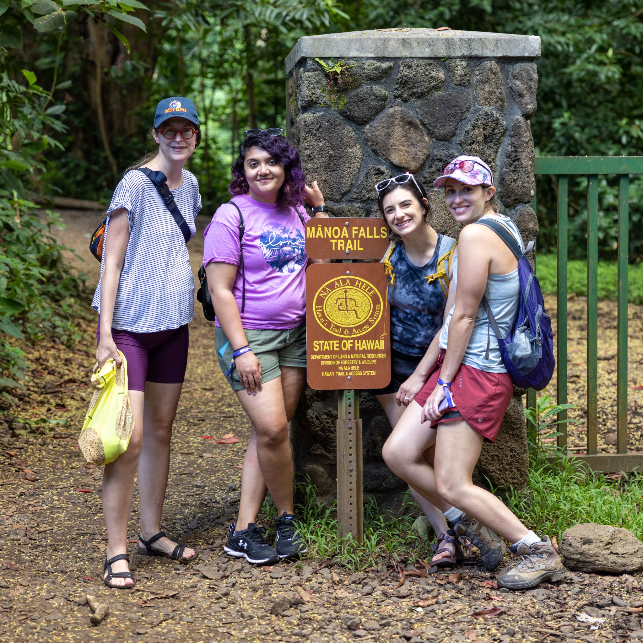 Four people standing at the trail marker for the beginning of the Manoa Falls Trail.
